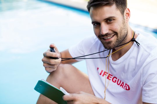 Lifeguard holding clipboard and stopwatch at pool
