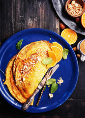 French pancakes - Crepe Suzette with orange syrup and hazelnuts on black wooden board. top view, copy space.