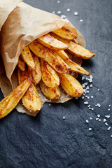 Baked potato fries with addition  sea salt on a black background, top view