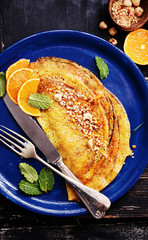French pancakes - Crepe Suzette with orange syrup and hazelnuts on black wooden board. top view, copy space.