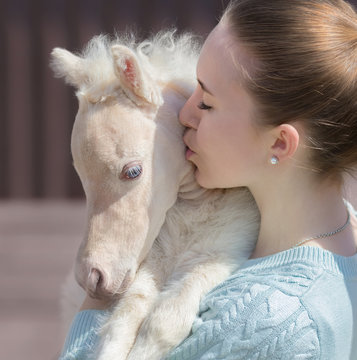 Young cute woman kissing miniature foal. Close up photo.