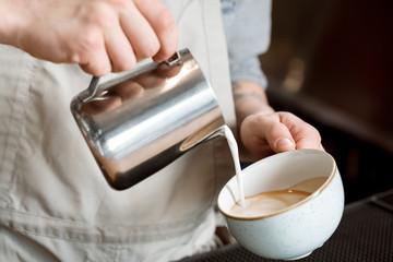 Almost done. Cropped closeup of a barista adding some steamed milk to the cup of coffee