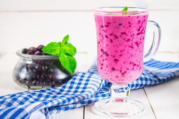 Smoothies of black currant in a glass with a handle on a white wooden table.