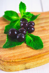 Black currant on a blackboard with a straw and smoothies on a white wooden table.