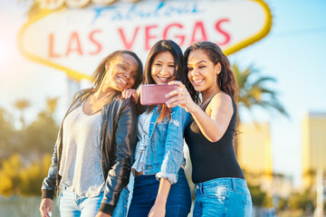 all girl group of friends having fun taking selfies in front of welcome to las vegas sign