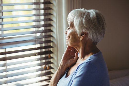 Thoughtful senior woman looking out from window - Powered by Adobe