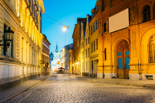Riga Latvia. Evening View Of Deserted Pils Street, Ancient Architecture In Bright Warm Yellow Illumination
