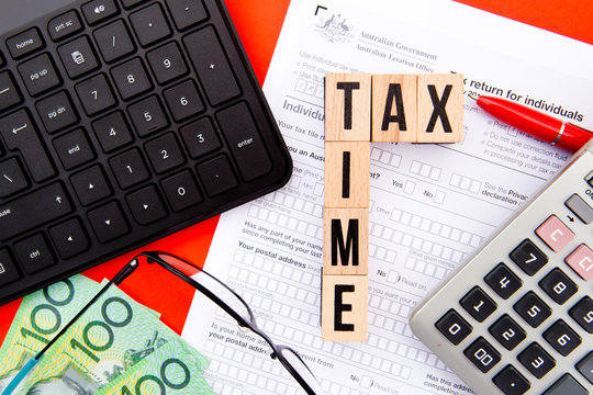 Tax Time - Australia - wooden letters with Tax Form, eyeglasses, money, keyboard and calculator
