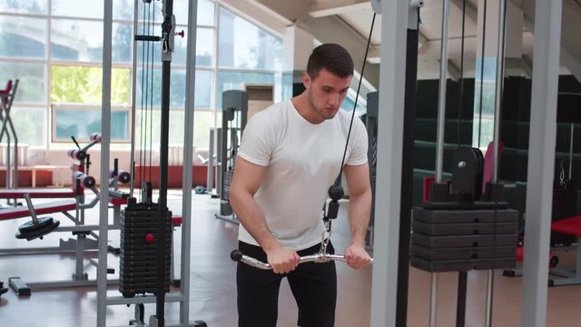Muscular man working out in gym doing exercises at triceps.