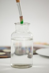 Paintbrush with green paint dipped into a jar filled with water