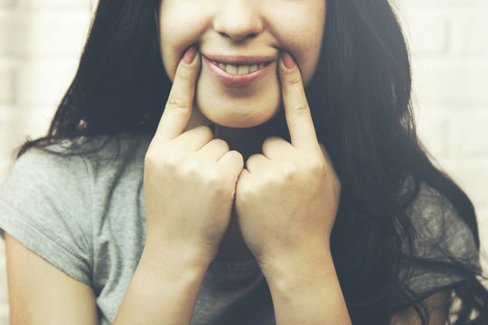 young sad girl forcing a smile with her fingers