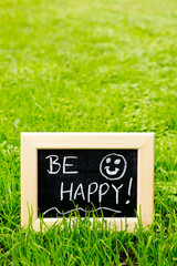 Be Happy handwritten in chalk on blackboard with green grass background
