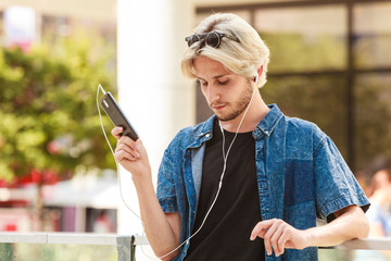 Hipster man standing on city street listening music