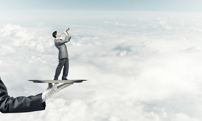 Businessman on metal tray playing fife against blue sky background