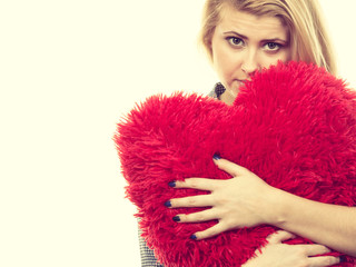 Sad girl holding big red pillow in heart shape