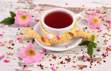 Cup of hot tea with wild rose flower on rustic wooden background
