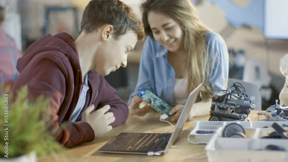 Poster girl and boy program electronic device with laptop for their science/ robotic/ engineering class at 