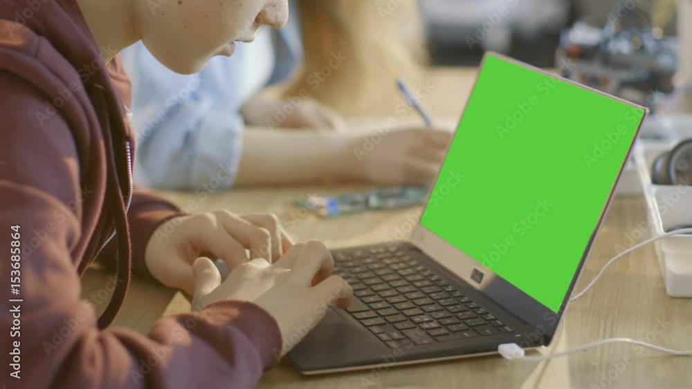 Aufkleber smart young boy works on a laptop with mock-up green screen in his computer science class. shot on r