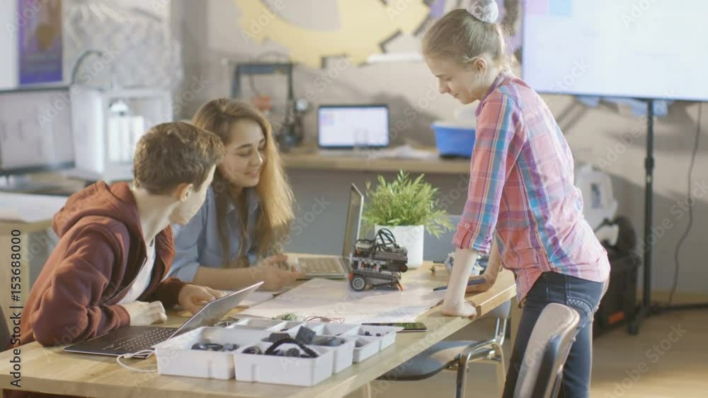 Poster boy and two girls working on a schools science class project. they draw, use laptop and build roboti