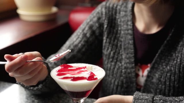 Cheerful girl having her dessert and green tea in a cafe. Woman eating panna cotta with a spoon