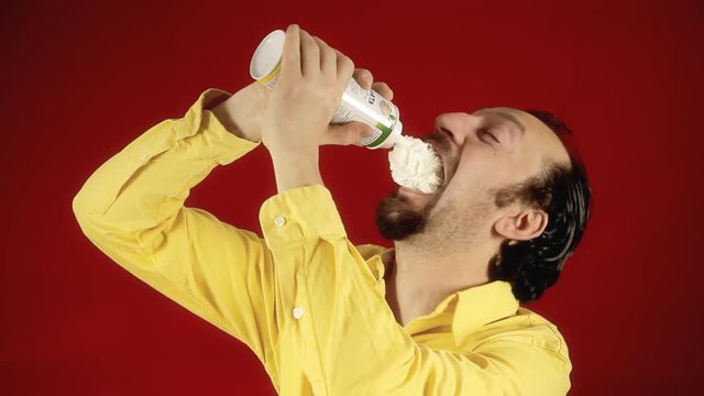 A funny ugly man sprays whipped cream directly into his mouth. Medium close-up shot.
