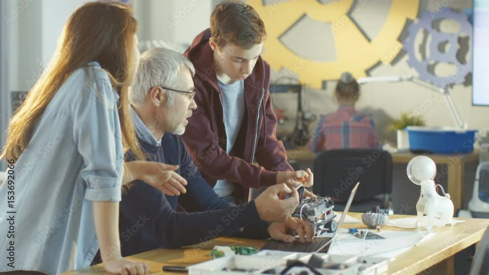 Poster in computer science class teacher examines programed robot made by girl and boy. shot on red epic-w 