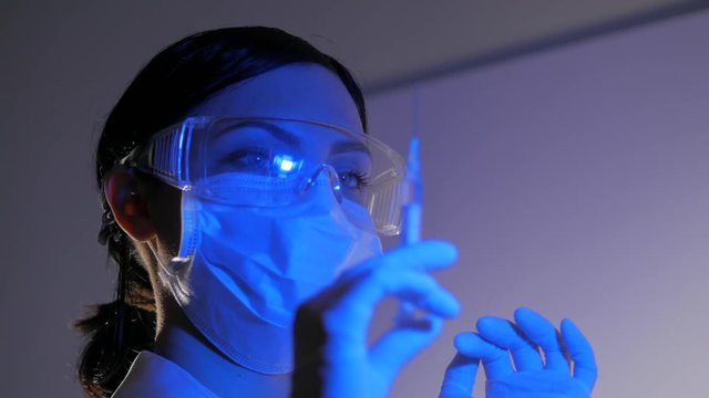 Nurse or doctor in gloves flicks syringe prior to drug injection, to collect and release the air out of the syringe. Healthcare and medicine concept.