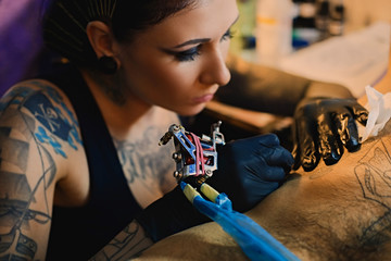 Close up image of female tattoo artist makes a tattoo on a man's torso.