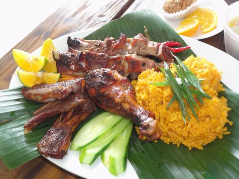 Chamorro beef and chicken barbeque meal with yellow rice in banana leaves Authentic Chamorro favorite cuisine of beef and chicken barbeque served with yellow rice, cucumber and lemon slices.