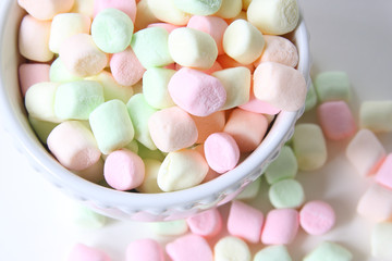 Multi-colored mini marshmallows in a white bowl, isolated on a white background