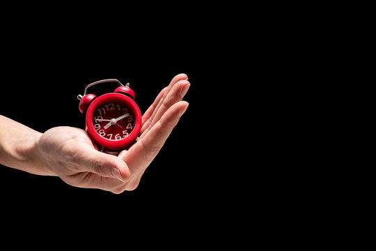 Male hand holding red alarm clock on a black background. Free space for text - Powered by Adobe