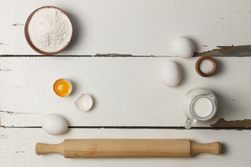 Baking background. Cooking ingredients for yeast dough and pastry, eggs, flour and milk on white rustic wood. Top view with copy space, mockup for menu, recipe or culinary classes.