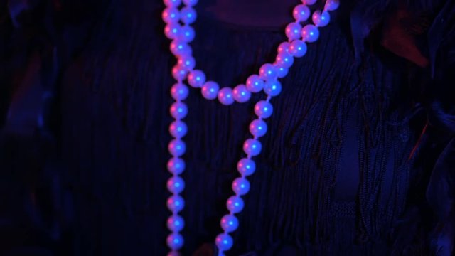 Woman dressed in the style of a Great Gatsby touches her pearl beads on party. Neon blue and red light.