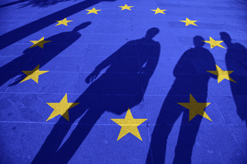 Fototapeta premium European Union flag painted on tiled street floor and shadows group of people walking at sunny day.