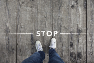 Man standing on the wooden boards with stop message on the floor, point of view perspective used. - obrazy, fototapety, plakaty