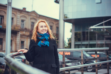 A woman in a European city  walks in a black coat at autumn and examines the neighborhood
