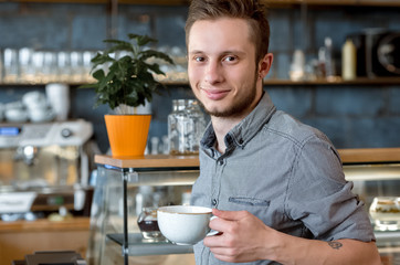 Quality checked personally. Shot of a young hipster man smiling to the camera holding a cup of coffee at the local coffee shop