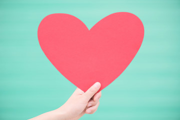 Symbol of Valentines day.Woman holding a red heart shape card with green background.