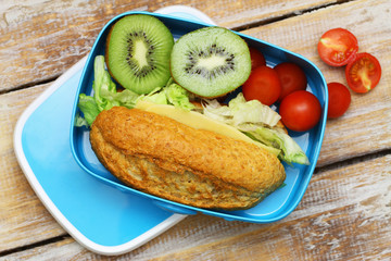 Healthy school lunch box containing wholegrain cheese sandwich, cherry tomatoes and kiwi fruit
