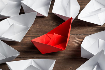 Business leadership concept with white and color paper boats on wooden table