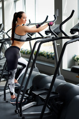 Fototapeta na wymiar Concept of sport and healthy lifestyle. Strong young beautiful woman is engaged in a gym on an ellipsoid. Woman is engaged in simulator