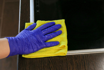Closeup on woman's hands in blue protective rubber gloves cleaning kitchen cabinets