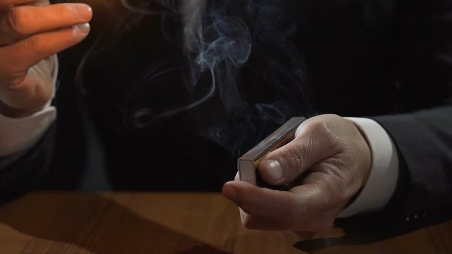Rich man in expensive suit lighting up Cuban cigar with a match, smoking male