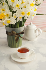 Breakfast still life, Cup of tea teapot, a bouquet of yellow flowers - daffodils and narcissus. Spring flowers background, vertical