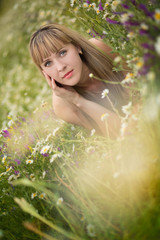Naklejka na ściany i meble Beautiful woman enjoying daisy field, nice female lying down in meadow of flowers, pretty girl relaxing outdoor, having fun, holding plant, happy young lady and spring green nature, harmony concept