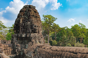 Fototapeta premium Smiling stone faces of Prasat Bayon, the central temple of Angkor Thom Complex, Siem Reap, Cambodia. Ancient Khmer temple is surrounded by tropical trees, famous Cambodian landmark, World Heritage.