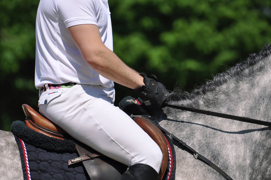 Fest im Sattel, Detailaufnahme von Reiter auf dem Pferd w&auml;hrend eines Springreitturniers