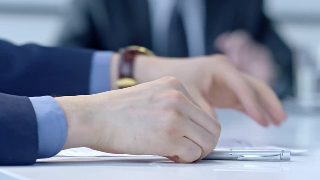 Closeup of hands of businessman taking document and signing it with pen while his colleague explaining something during office meeting