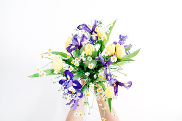 Girl's hands holding beautiful flowers bouquet: tulips, chamomiles, iris flower on white background. Flat lay, top view. Floral composition