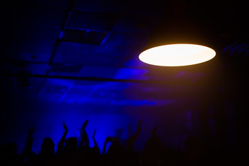 Fototapeta premium Audience with hands raised at a music festival and lights streaming down from above the stage.